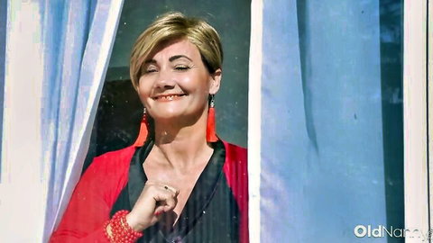 Lacey Starr mature blonde smiling in red cardigan by window