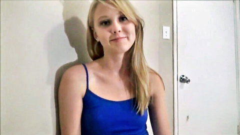Smiling blonde teen in tight blue tank top posing against bathroom door