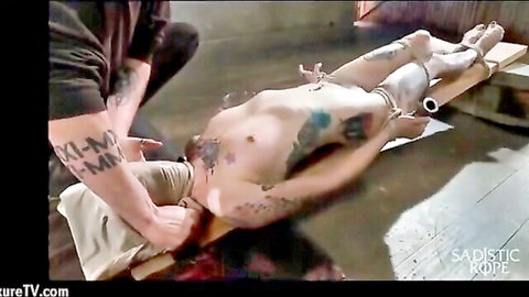 Tattooed man bound in ropes for sadistic BDSM torture session