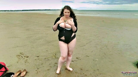 Busty brunette squeezing huge natural tits in revealing black swimsuit on beach