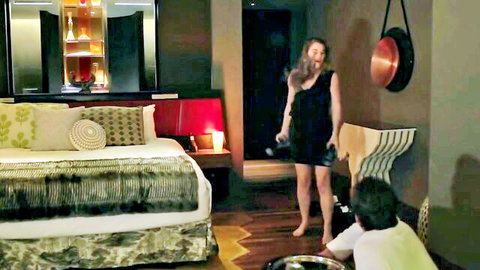 Sexy fit babe in short black dress stands over kneeling guy in luxurious bedroom