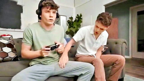 Two young gay twinks in casual clothes, one gaming as the other approaches intimately