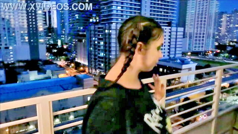 Brunette with braids overlooking Miami skyline at night on balcony