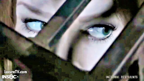 Intense blue-eyed woman peering through metal restraints in BDSM scene