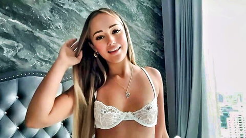 Smiling blonde in sheer lace bra showing cleavage on webcam bed