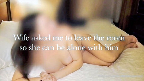 Blurry hotwife scene: mature Asian woman topless on bed, legs spread, asking husband to leave for alone time