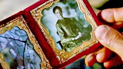 Hand holding open ornate red locket revealing vintage sepia photos of curly-haired woman in green dress
