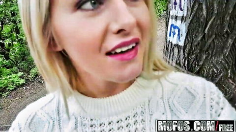 Blonde babe with pink lips smiling seductively outdoors in white sweater