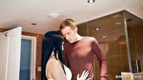 Busty black-haired wife in tight white tank top passionately kisses husband in maroon shirt by shower