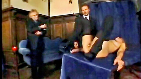 Blonde submissive slave spreads legs exposing pussy to two suited doms in BDSM scene