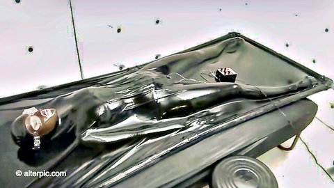 Latex-clad woman mummified in plastic wrap for intense BDSM fetish scene
