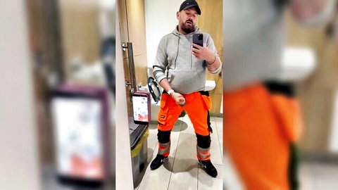 Bearded construction worker pulls down orange pants exposing thick uncut cock in public restroom selfie
