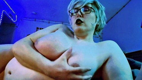 Thick mature woman with glasses squeezing her huge bare tits in neon blue light