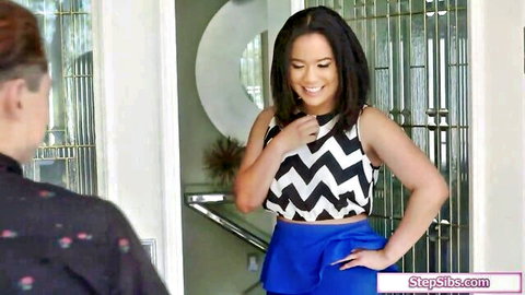 Smiling brunette stepsister in zigzag tank top and blue skirt teasing at doorway