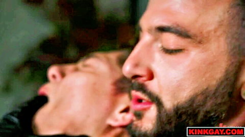 Bearded gay submissive in leather collar with mouth agape endures intense domination close-up