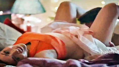 Indian woman in orange top and white skirt teases on bed with partner