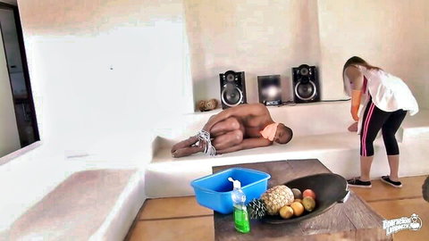 Skinny fair white maid in leggings stands over bound naked muscular black man on couch