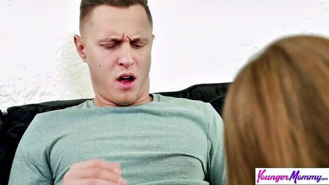Shocked young Caucasian guy in green shirt gawks at redhead stepmom's back on couch in taboo scene