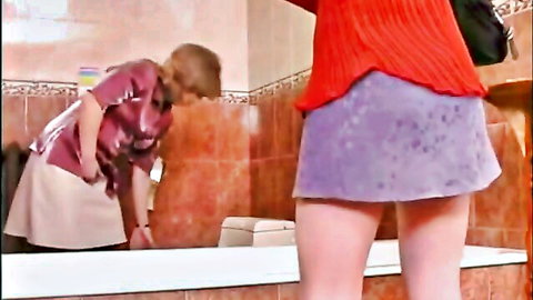 Mature woman in short skirt bends over mirror, seduced by younger in lesbian tease