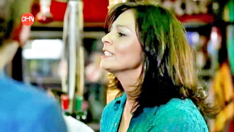 Seductive brunette MILF in teal blouse smiling in erotic comedy scene