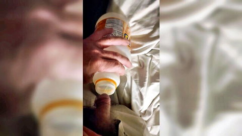 Blurry amateur male holding sports bottle near exposed penis on bed