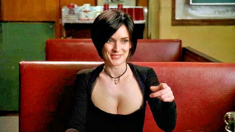 Winona Ryder in low-cut black top showing cleavage, pointing seductively