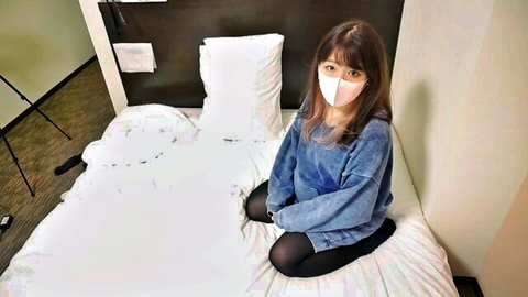 Cute masked Asian girl sitting on bed in blue sweater and black leggings