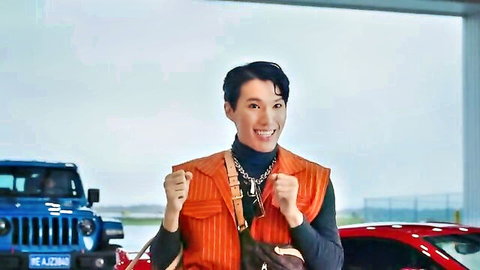 Asian man in orange vest posing excitedly near cars, Joy Ride 2023 celeb scene