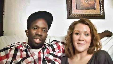 Smiling ebony man in plaid shirt and redhead woman cuddling on living room couch