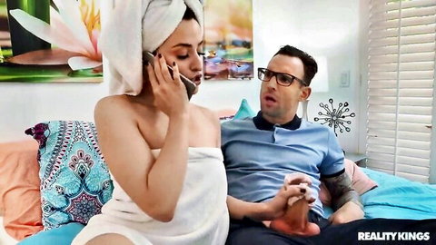 Skinny brunette in towel talks on phone while guy holds her foot on bed