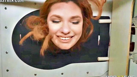 Smiling redhead with freckles pokes face through gloryhole wall hole