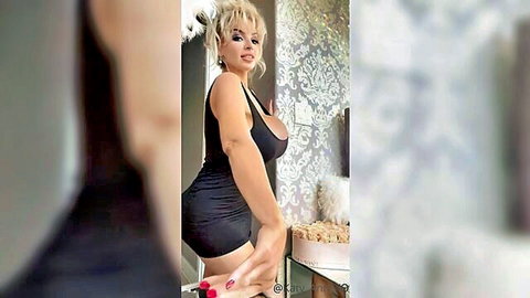 Platinum blonde bimbo in tight black dress showing huge cleavage
