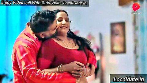 Indian man embraces mature woman from behind, intimate kiss in red blouse