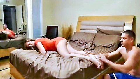 Step sister in red swimsuit gets foot massage from step brother on bed