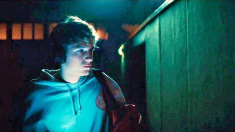 Young man in blue hoodie and headphones, intense gaze in dim night scene from Euphorie S01E05