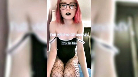 Pink-haired e-girl in glasses teases with fishnet legs spread wide on bed in strapless top