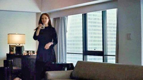 Mature brunette woman in tight black dress sips cocktail seductively by hotel window