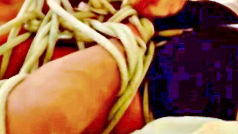 Muscular young man tightly bound with thick ropes around arms and chest in gay bondage