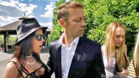Rocco Siffredi walks with brunette in revealing black top and blonde in white dress outdoors