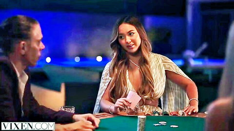 Sexy Asian babe with big tits in revealing dress holding poker cards at casino table