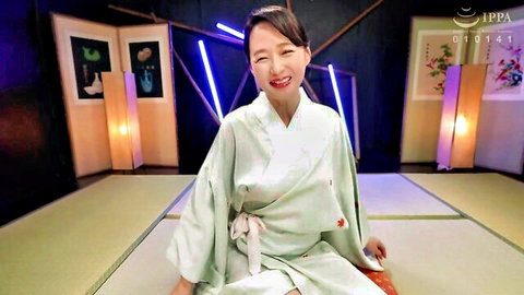 Smiling Asian MILF in light green kimono sitting on tatami mat in bedroom