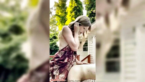 Blonde trans woman in dress dominating bent-over man outdoors