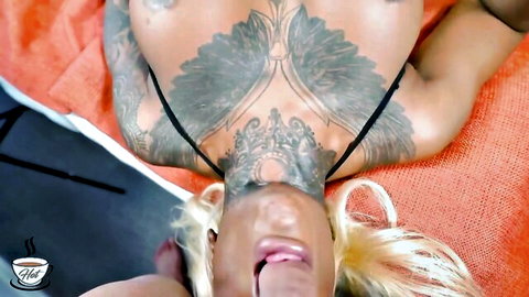 Tattooed busty blonde lies back exposing massive inked tits with tongue out POV