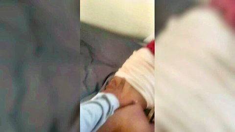Blurry closeup of hand gripping small black woman's thigh in white shorts on bed