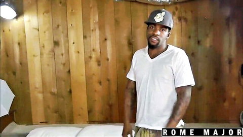 Rome Major in white V-neck tee and hat, posing confidently