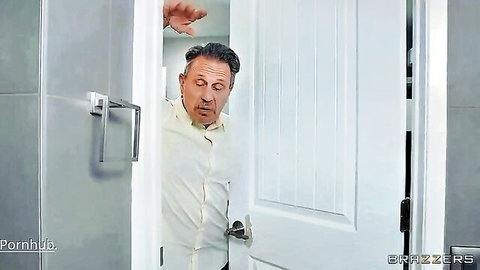 Excited middle-aged man in white shirt peeking through open bathroom door in Brazzers scene