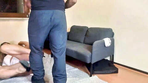 Tattooed ebony hunk in sweatpants stands over naked muscular white guy with legs spread on floor
