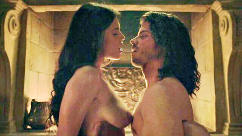 Topless brunette with bare tits passionately kissing muscular long-haired man by fireplace