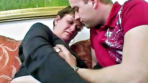 Mature MILF in suit intimately embraced by man on couch
