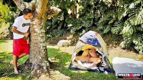 Tattooed guy in red shorts watches woman's bare ass and pussy exposed in open camping tent outdoors